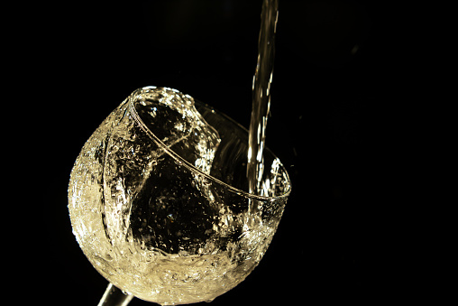 Stream of white wine falling on a glass and producing splashes on black background