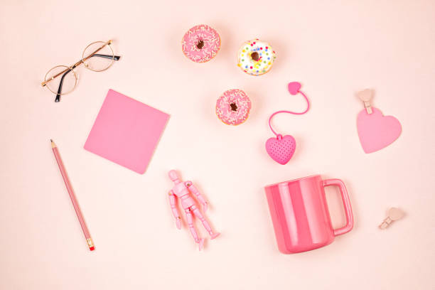 Flat lay with pink accessories, tea cup and donuts over light pink background. Top view. Morning rituals, stay at home idea
