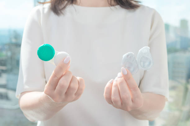 A woman holds reusable lenses in one hand and one day contact lenses in the other. choosing contact lenses A woman holds reusable lenses in one hand and one day contact lenses in the other. eyesight problem concept eye test equipment stock pictures, royalty-free photos & images