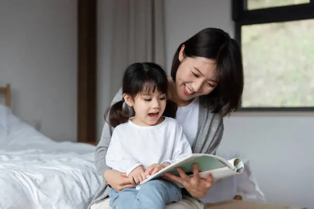 Photo of Young Asian mother is reading a book with her daughter