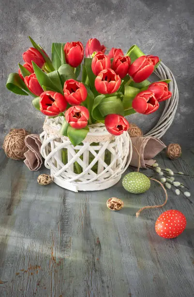 Easter greeting card design with bunch of red tulips on rustic background with Easter decorations, space for your text.
