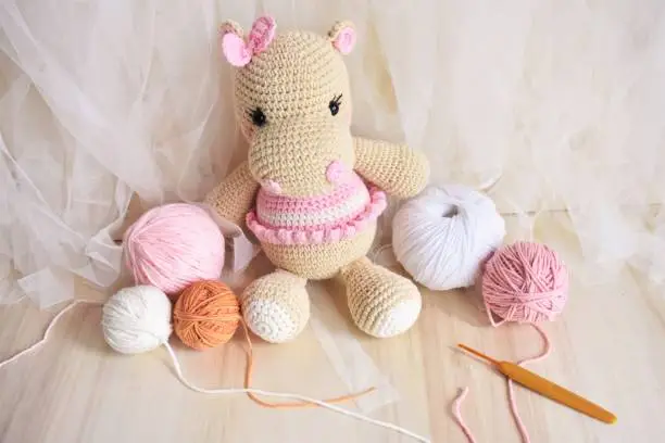 Photo of Cute hippopotamus crochet handmade toys for kids. Vintage background soft toy for children. Hippo knitting, Handmade Hippie, woolen Hippie baby. Wool and crochet hook, pink pastel background. Crocheting animals for decorating on bedroom of child. Home dec