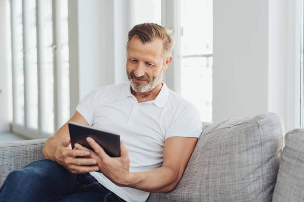 człowiek relaksujący się w domu ze swoim tabletem pc - sofa men sitting contemporary zdjęcia i obrazy z banku zdjęć