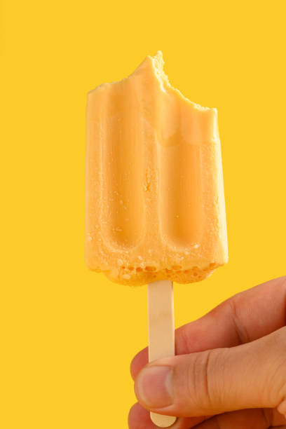 istock hand holding mango pudding flavor popsicle with couple of bites on a yellow background 1248882234