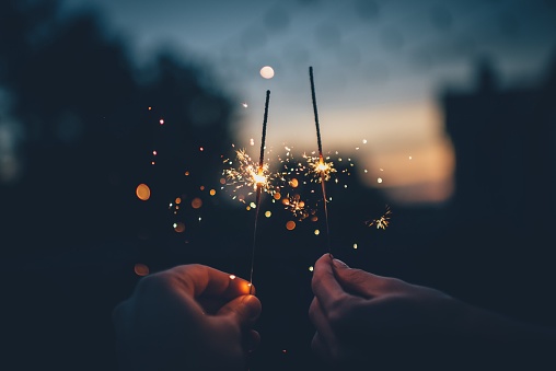 A close-up of two sparklers held by two people in hands.