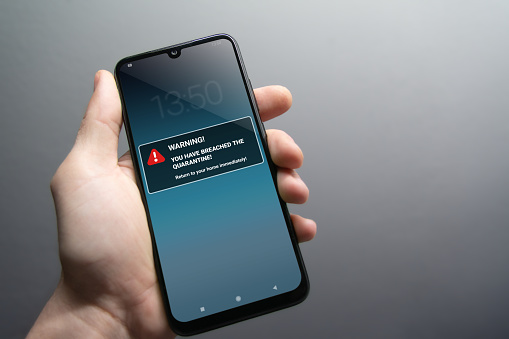 Quarantine breach alert mockup on smartphone being held in hand. Advice to stay in home quarantine to stop contagion. Pandemic, healthcare, technology and privacy