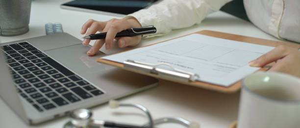 istock Female doctor writing medical certificate on laptop while looking information on patient chart 1248887397