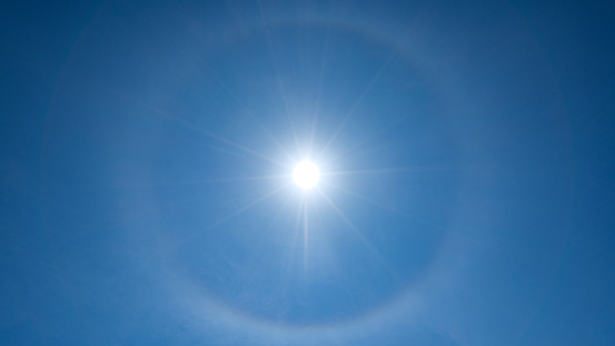 The glowing sun in the sky with a corona ring around it
