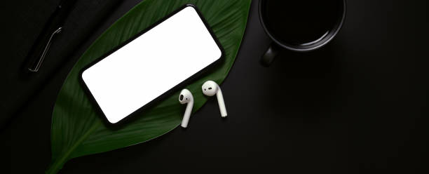 istock Blank screen smartphone, wireless earphone above leaf and coffee cup on dark background 1248887873