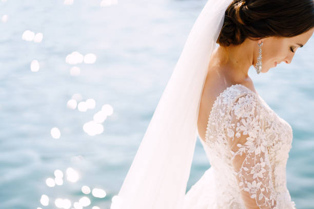 plan rapproché du cou et du cou de la mariée, profil de visage. belle grande boucle d’oreille dans les oreilles, épaule avec robe blanche de dentelle sur le fond de l’éblouissement de l’eau. photo de mariage d’art au monténégro, perast. - boucle doreille photos et images de collection