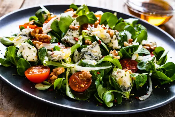 Fresh salad - blue cheese, cherry tomatoes, spinach, walnuts on wooden background