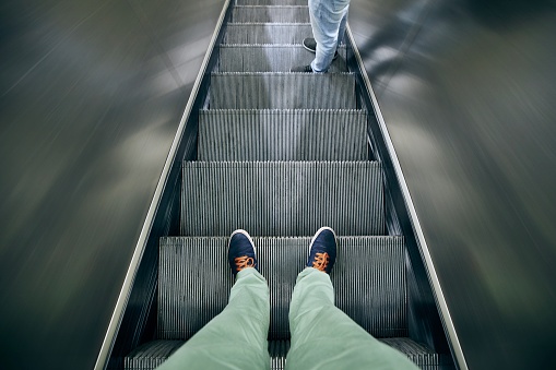 Social distancing during daily life. Low section of two men standing on escalator.