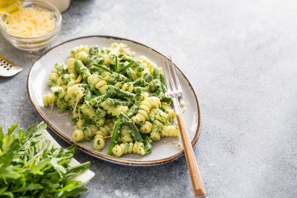 pasta with green vegetables and creamy sauce. fusilli pasta with asparagus beans and spinach on grey stone background stock photo