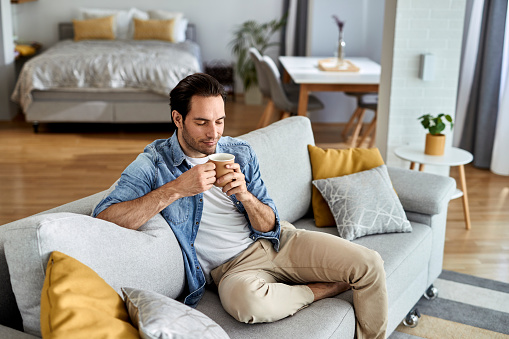 Smiling man enjoying in smell of fresh coffee while relaxing with his eyes closed at home.