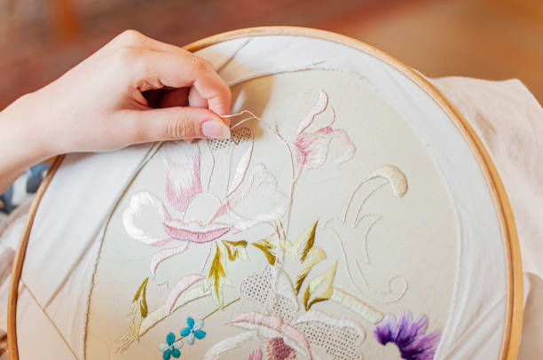 A woman's hand holding a needle embroidering some flowers and leaves onto natural linen.