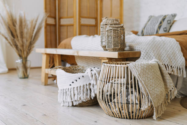 Comfortable bedroom in bohemian interior style with furnishing Selective focus on home decor. Comfortable bedroom in bohemian interior style with textile sheet on bed, wooden bench seat, bamboo dressing screen, dry plants in vase, wicker basket bed decoration stock pictures, royalty-free photos & images