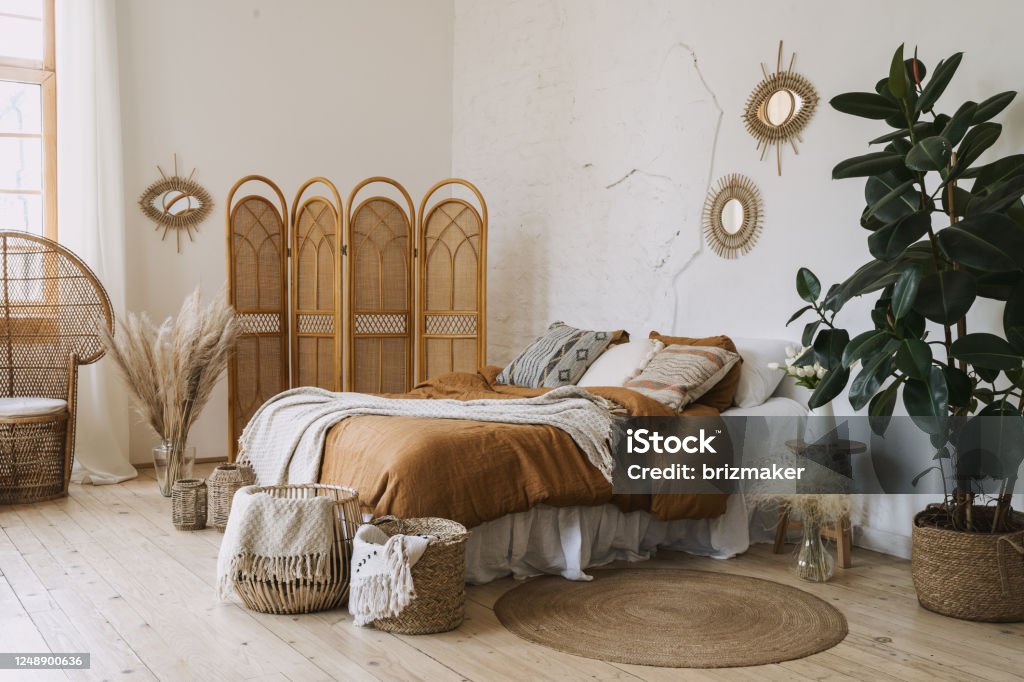 Comfort apartment in bohemian style interior with hygge bedroom Comfortable apartment in bohemian style interior with hygge bedroom, pillow and bedspread on bed, bamboo dressing screen, home decor, dry plants in vase, wicker basket, houseplant on floor Bedroom Stock Photo