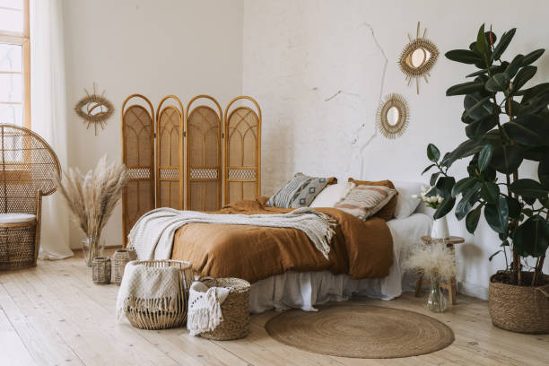 Comfort apartment in bohemian style interior with hygge bedroom Comfortable apartment in bohemian style interior with hygge bedroom, pillow and bedspread on bed, bamboo dressing screen, home decor, dry plants in vase, wicker basket, houseplant on floor bamboo material stock pictures, royalty-free photos & images