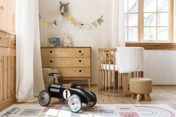Comfortable kid bedroom in bohemian interior style with home decor, wooden chest of drawers, retro car toy and cozy sleeping baby place