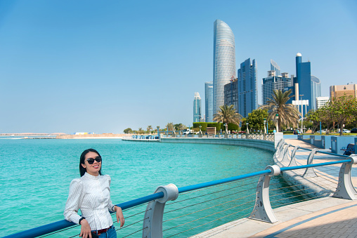 Female Asian tourist visiting Abu Dhabi downtown corniche area and enjoying the view in the United Arab Emirates capital city