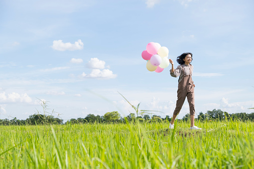 Happy Asian young girl holding balloon running at beautiful field rice, Nature background.