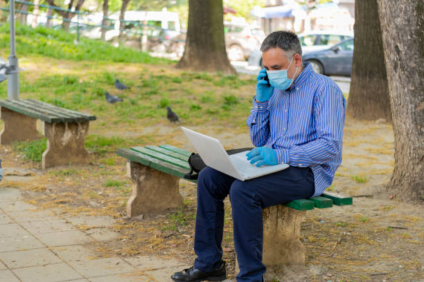 istock Avoiding the Virus Outbreak. Businessman Working on Laptop in the Park and Communicating via Smart Phone. 1248916174