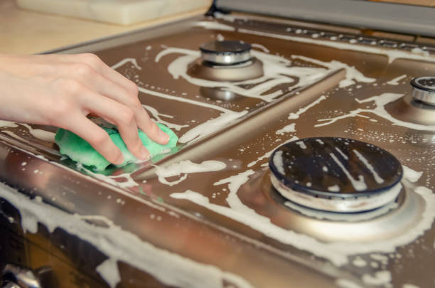 女性の手は緑の泡のスポンジと灰色のステンレス鋼のガスストーブを打つ。ハウスクリーニング - burner ストックフォトと画像