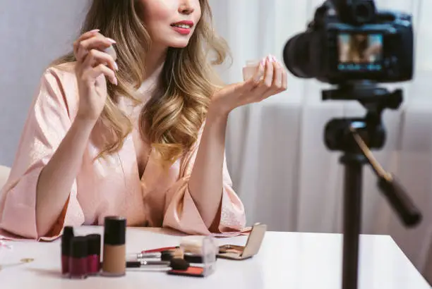 Famous blogger. Young attractive woman fashion vlogger talking to the camera about skin care products and cosmetics while recording vlog. New eco friendly handcream. Healthy lifestyle beauty blog