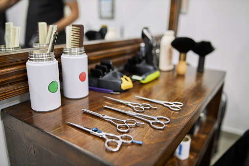 Hairdresser work tool, scissors, brush, and spray bottles on a wooden hairdressing table in barber shop