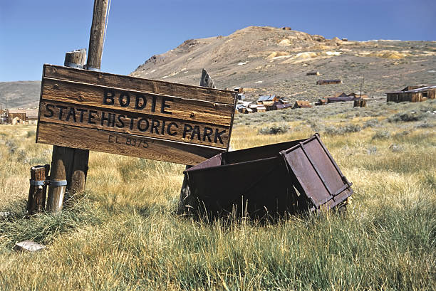 Bodie State Historic Park is a  preserved California gold-mining ghost town. Items inside the buildings are in a natural, dusty condition. This sign is at the entrance to the park. Some of the old buildings are visible in the background. Taken with a Olympus OM4T, scanned and finished in Photoshop.