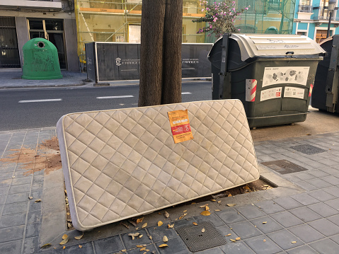 Valencia, Spain - June 9, 2020: Old used mattress left in the street leaning on tree. Sometimes people leave things like this in the street hoping someone that needs it will grab it. It is easier than trying to dispose it properly