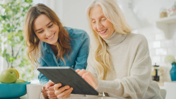 piękna wnuczka uczy babci używać tabletu. autentyczna starsza kobieta przegląda internet i pisze teksty na gadżet. wartości rodzinne w epoce technologicznej. - family domestic life senior adult computer zdjęcia i obrazy z banku zdjęć