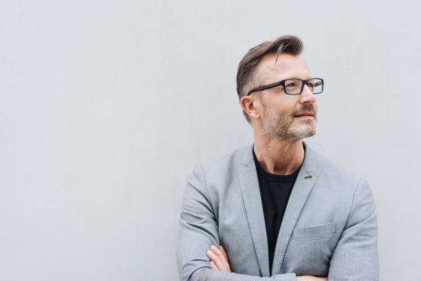 Mature man with glasses wearing grey jacket Portrait of mature man wearing grey jacket standing against white wall with copy space side view stock pictures, royalty-free photos & images