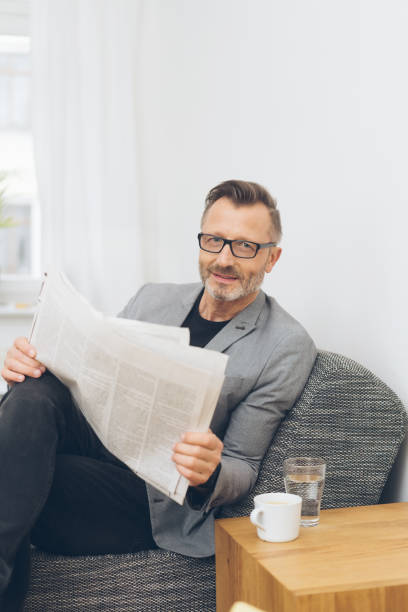istock Mature man reading newspaper while sitting on sofa 1248945624