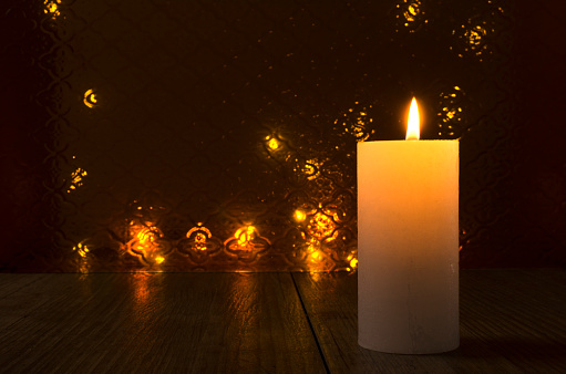Vertical image.Closeup of candle and flame of it against glass brown background, lights bokeh