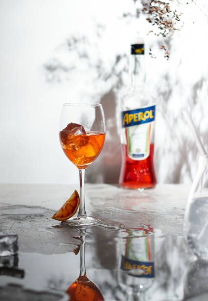 erfrischender aperol spritz cocktail und orange in scheiben geschnitten mit einer flasche aperol auf dem hintergrund - sonnenlicht und reflexionen - editorial eastern europe europe reflection stock-fotos und bilder