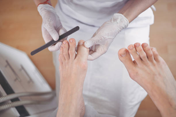 pedicurist che fa una procedura di pedicure medica professionale nel salone di bellezza usando la lima per unghie. trattamento del piede nel salone spa. clinica di pododiatria. le mani del medico estetista in guanti bianchi con le gambe femminili - pedicure podiatrist human foot moisturizer foto e immagini stock