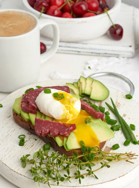 toast with poached egg and avocado on a round board, ripe red cherries