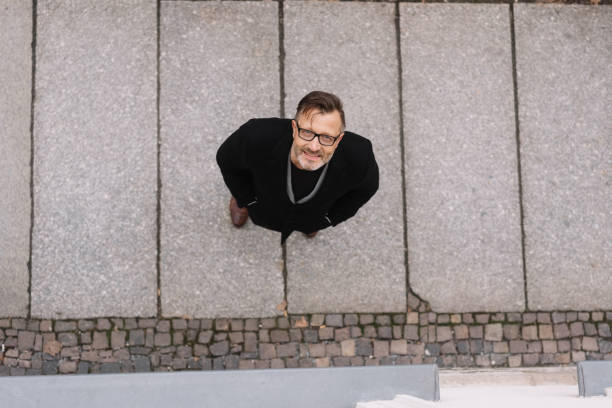 Smiling man wearing glasses and warm coat standing on concrete looking up from below with copy space