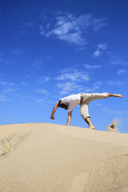 retrato de joven parkour hombre haciendo flip o somersault en la arena.joven hombre haciendo somersault rueda de carro al aire libre en la playa de arena - back somersault fotografías e imágenes de stock