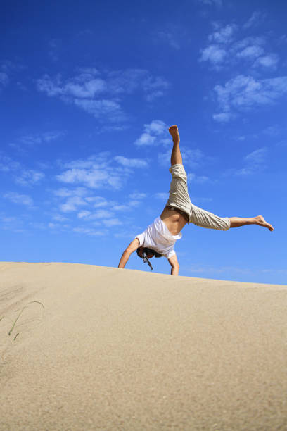 retrato del joven parkour hombre haciendo voltereta o salto en la arena.joven haciendo somersault rueda de carro al aire libre en la playa de arena. - back somersault fotografías e imágenes de stock