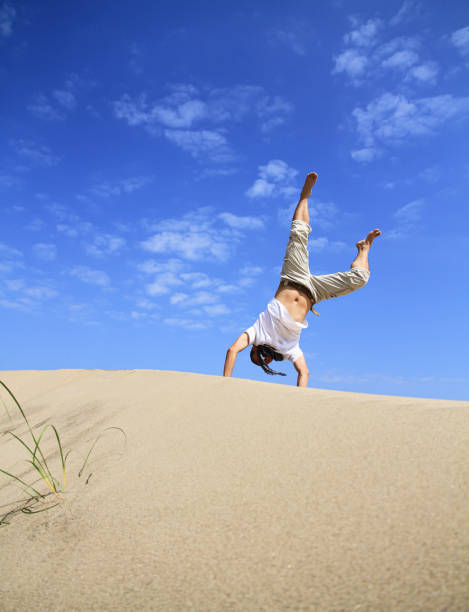 retrato do jovem parkour homem fazendo flip ou somersault na areia.jovem fazendo roda de carrinho de cambalhota ao ar livre na praia de areia. - back somersault - fotografias e filmes do acervo