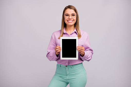 Portrait of positive cheerful girl promoter hold new device novelty tablet, suggest select ads promo wear good look clothes isolated over gray color background