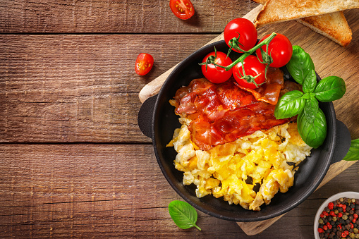 American breakfast with scrambled eggs and roasted bacon on wooden background. Top view.