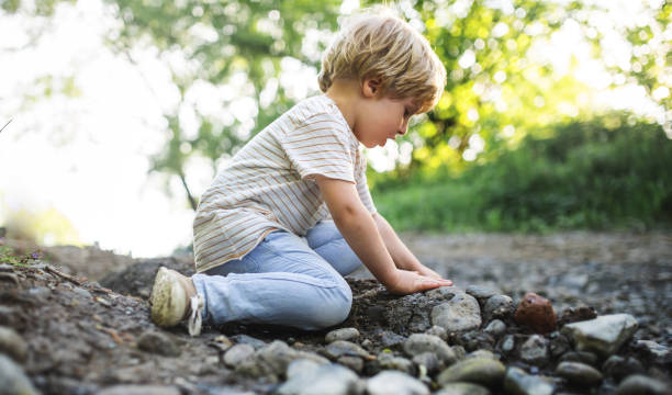 istock Side view of small boy playing with rocks and mud in nature. 1248961834