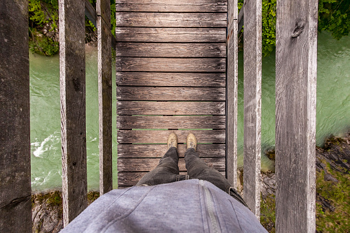 A man stands on a suspension wooden bridge in the mountains. Top view.