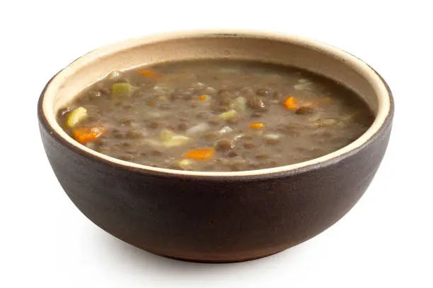 Lentil soup in a brown ceramic bowl isolated on white.