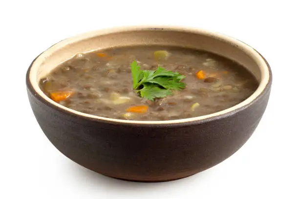 Lentil soup in a brown ceramic bowl isolated on white. Parsley garnish.
