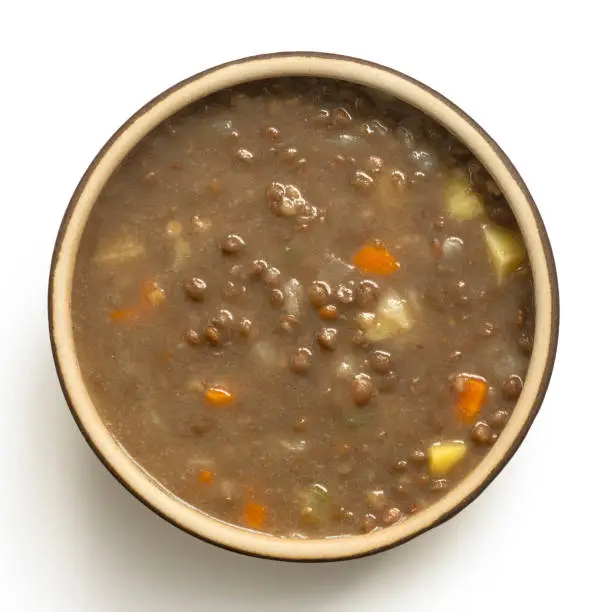 Lentil soup in a brown ceramic bowl isolated on white. Top view.
