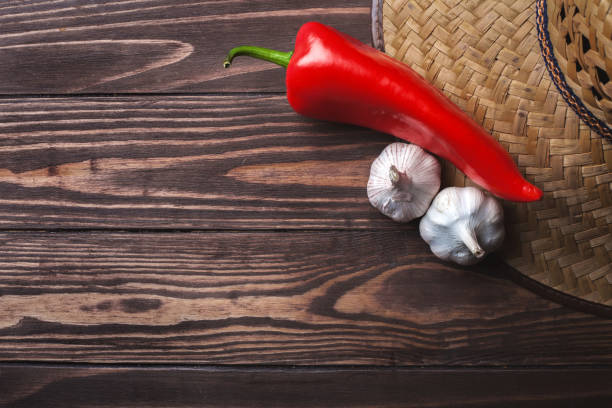 Pepper and garlic next to a sombrero straw hat on a textured wooden board with copyspace. flat lay
